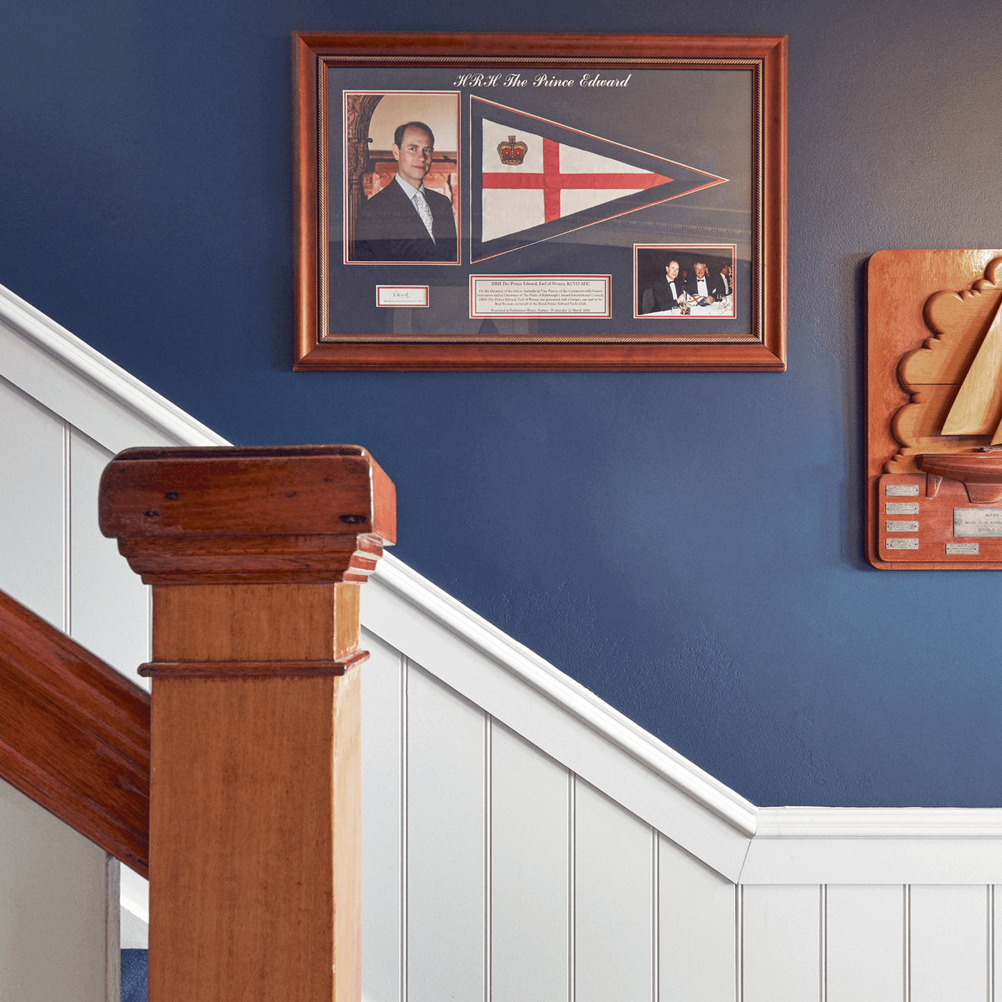 An image showcasing a framed image of Prince Edward and a flag in the club staircase.